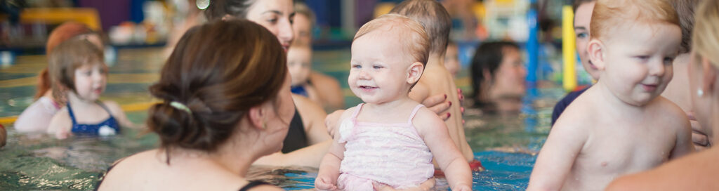A group of mothers holding their children in the pool as they learn to swim