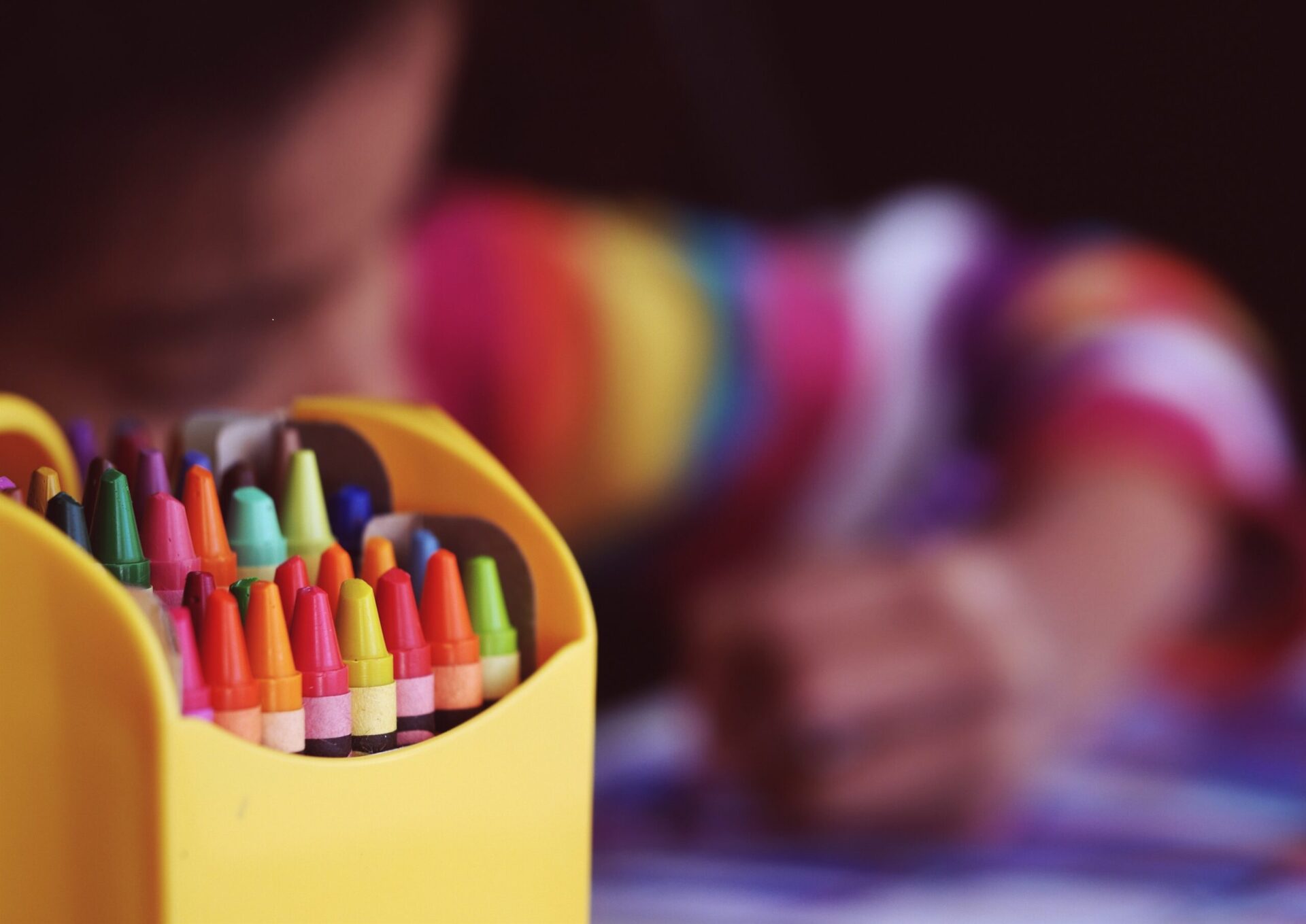 A box of crayons in front of a blurred child coloring