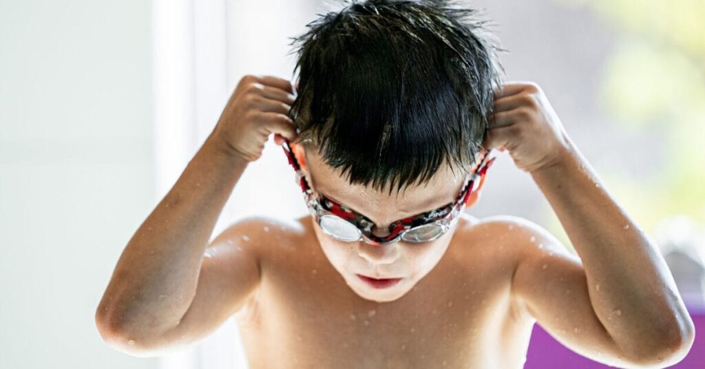 Child securing swimming goggles over his eyes and head.
